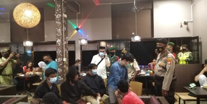 
					Ket foto: Tim gabungan Covid-19 Kabupaten Karimun berikan imbauan kepada pengunjung  anak muda yang tengah asyik nongkrong di kedai kopi Batam Bakery saat patroli social distancing. (James N). 